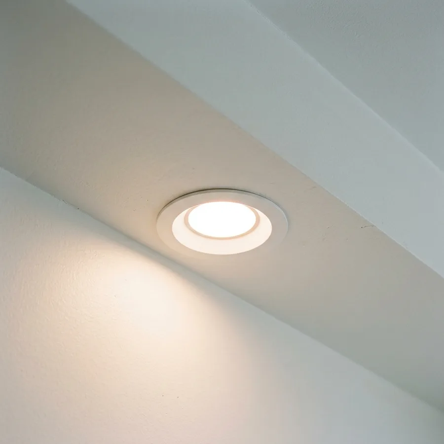 a newly installed LED recessed light glowing warmly in a finished ceiling, architectural detail shot, no people, clean drywall ceiling